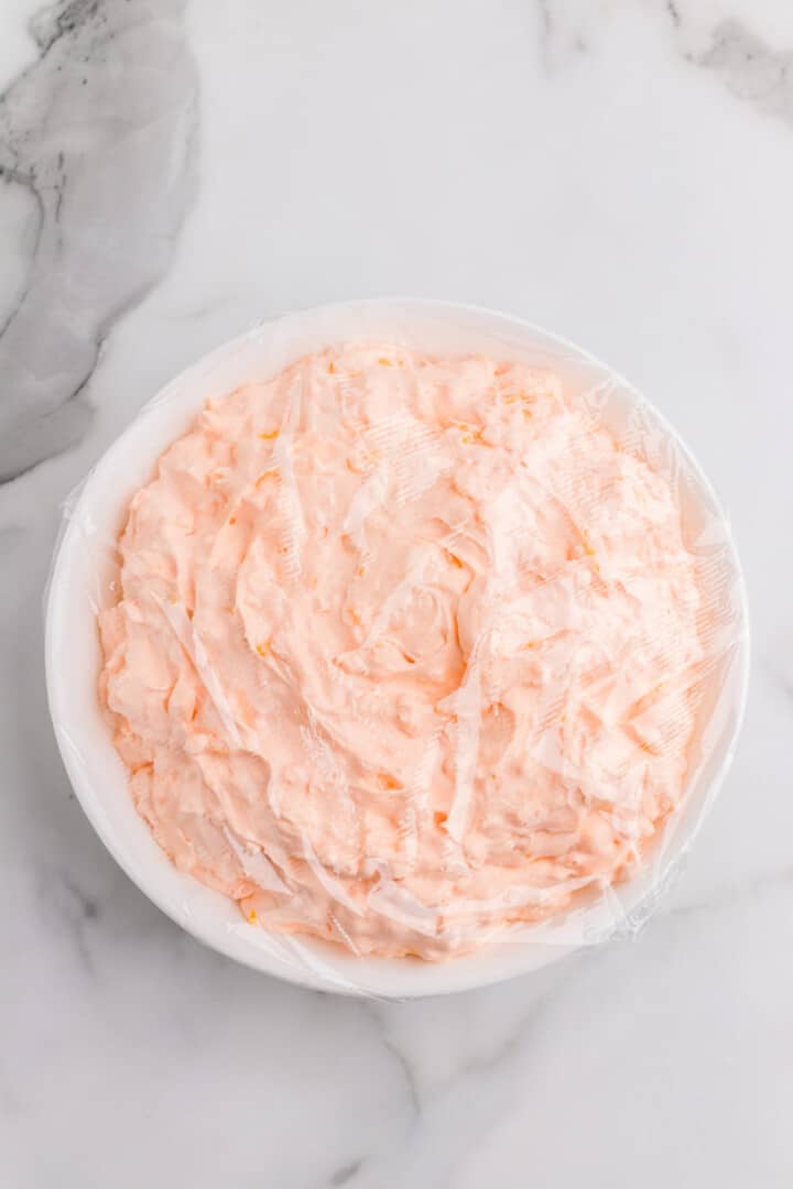 Orange Fluff in white bowl and covered with plastic wrap.