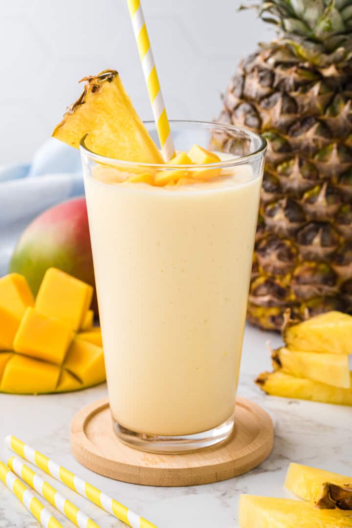 Mango Pineapple Smoothie in glass garnished with mangoes and pineapple slice.