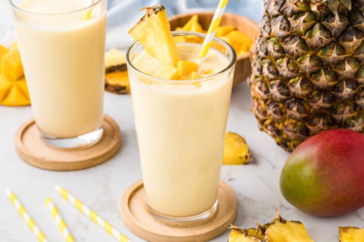 two smoothies in a glass on wooden coasters.