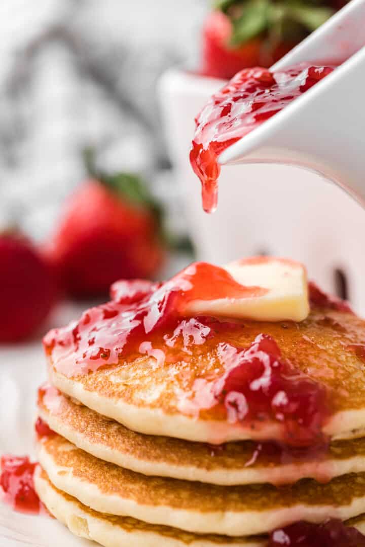 pouring the strawberry syrup on top of the pancakes.