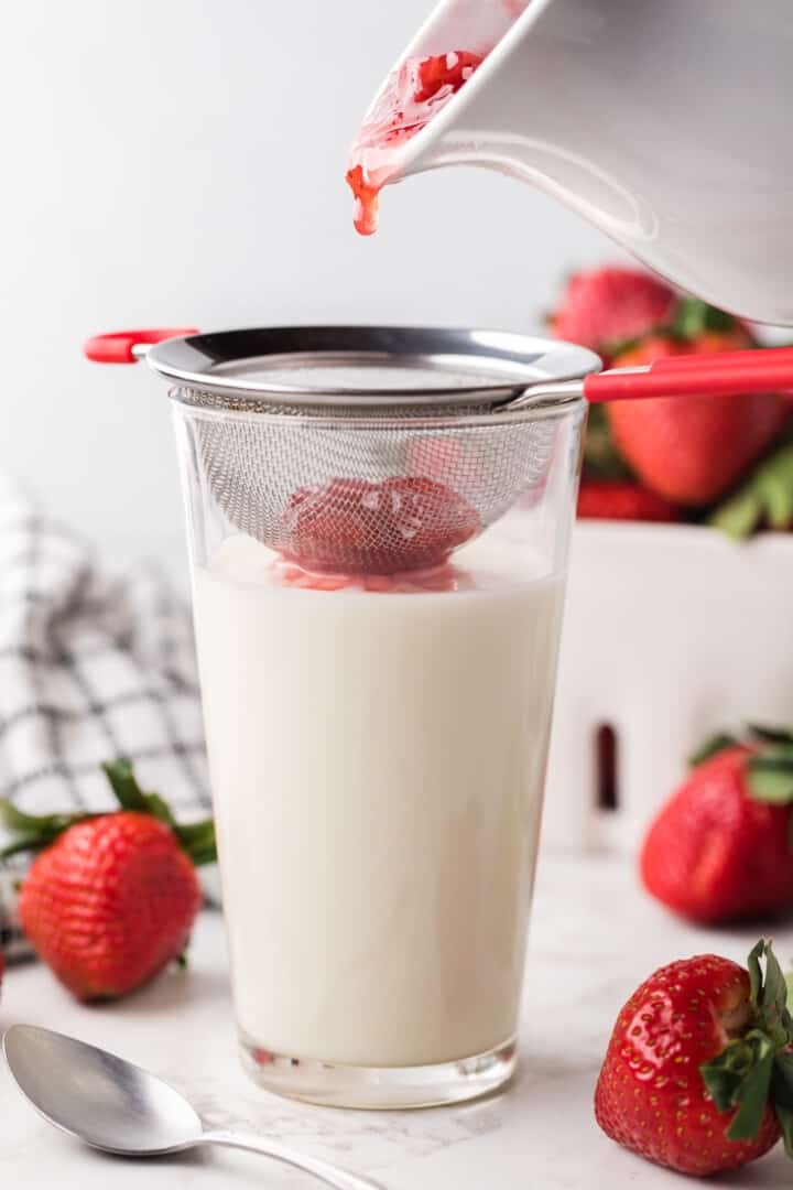 straining strawberry syrup to make strawberry milk.