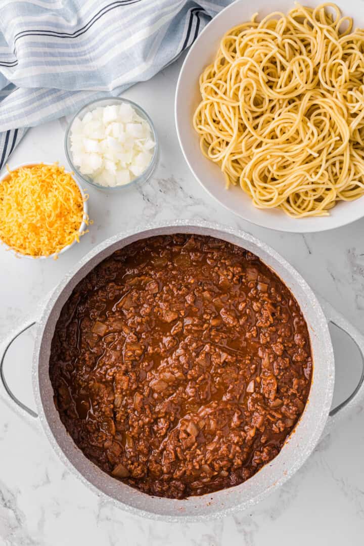 cooked Cincinnati Chili with onions, cheese and noodles for serving.