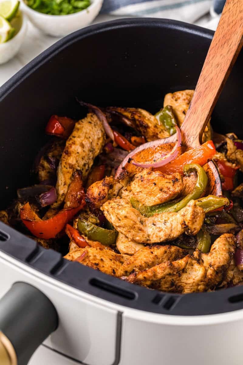 serving the air fryer chicken fajitas with a wooden spoon.