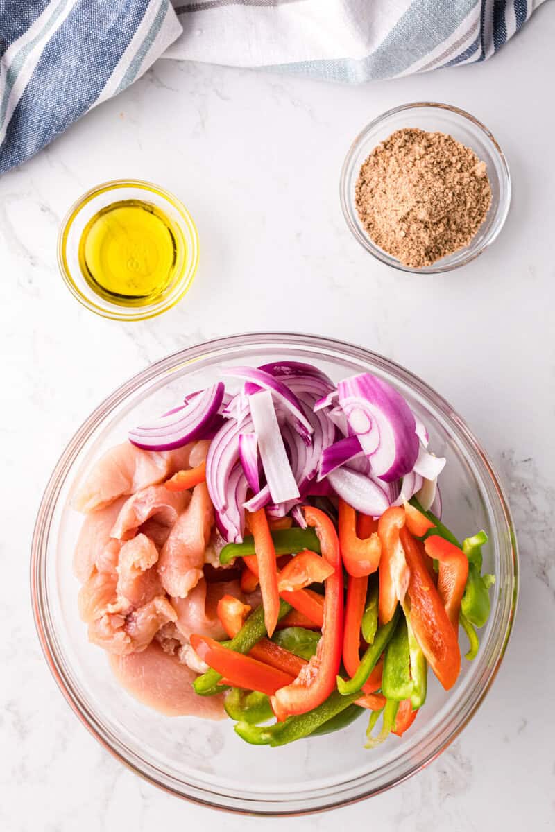 sliced chicken peppers and onions in a glass bowl.
