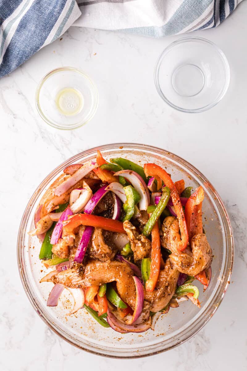 chicken and veggies mixed in a glass bowl with the oil and seasoning.