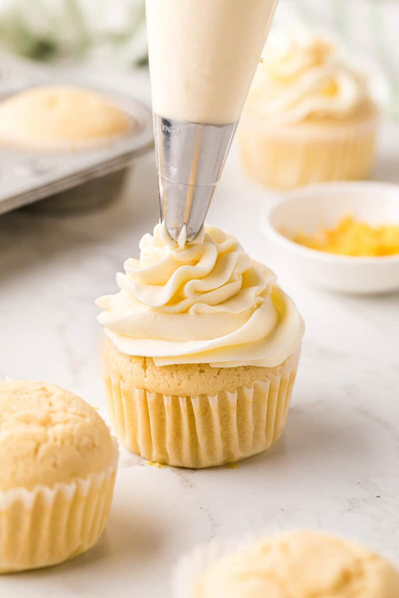 topping a lemon cupcake with the frosting.