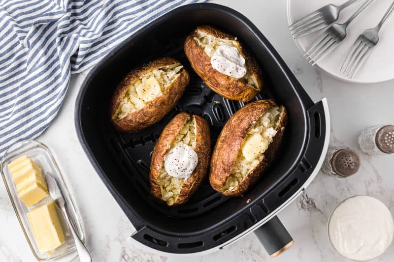 Four potatoes in the air fryer topped with butter and sour cream.