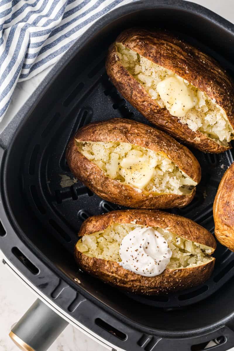 Baked Potatoes in the Air Fryer cut open with potatoes topped with butter and sour cream.