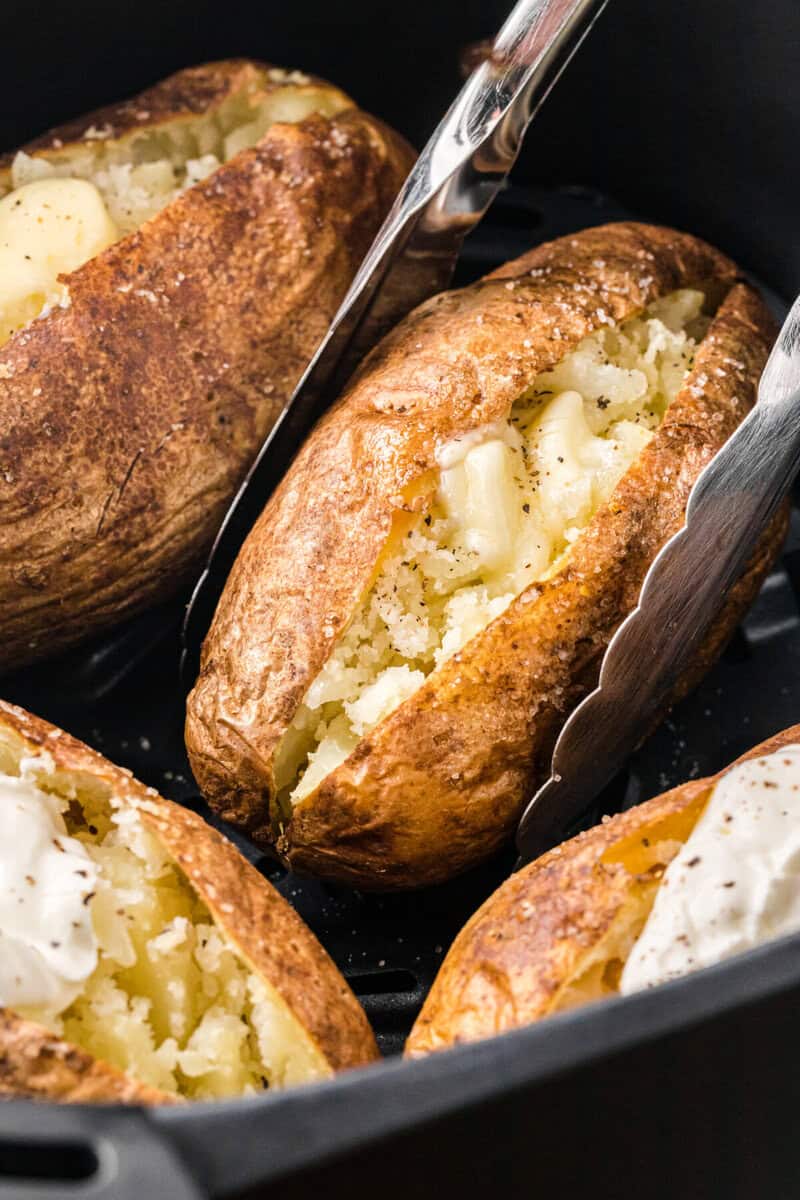 serving the baked potatoes out of the air fryer with tongs.