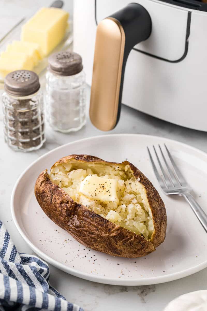baked potato served on white plate topped with butter.