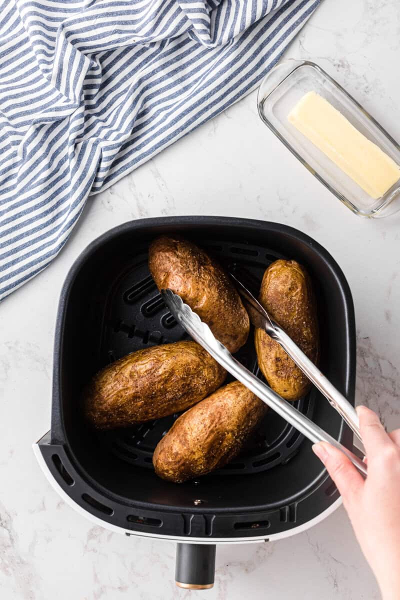 using tongs to flip the potatoes in the air fryer.