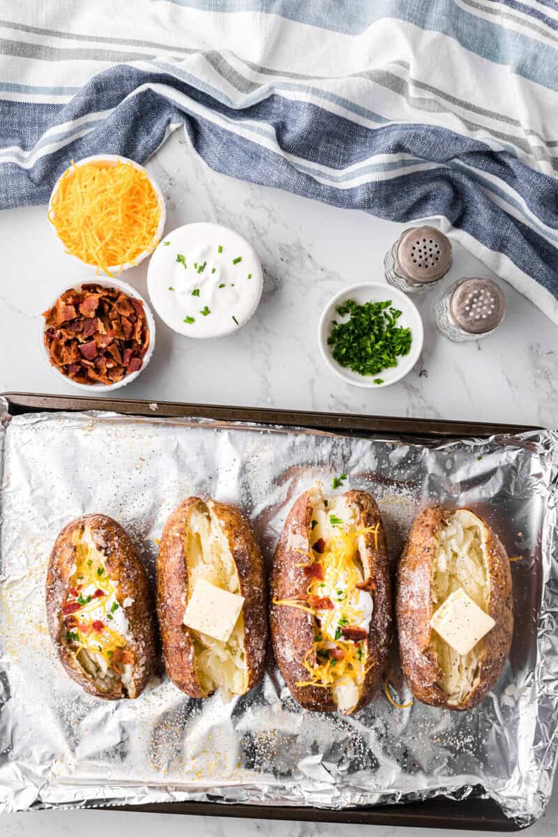 baked potatoes on baking sheet loaded with toppings.