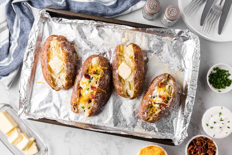 baked potatoes on baking sheet loaded with toppings.