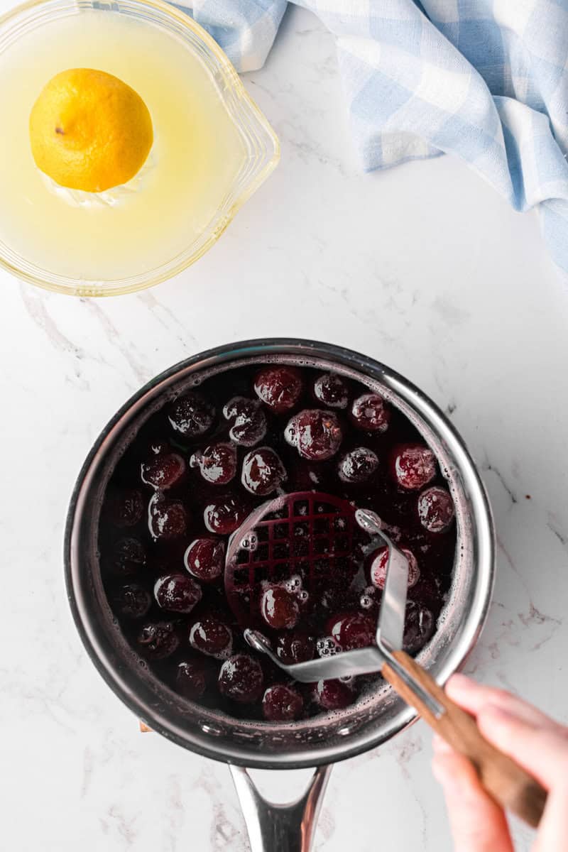 mashing the boiled cherries with a potato masher.