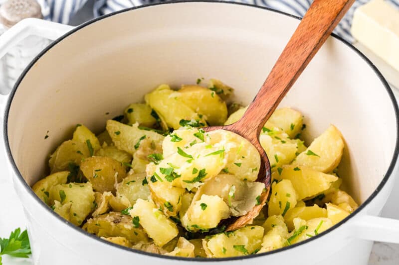 Parsley Potatoes being served with a wooden spoon out of a white pan.