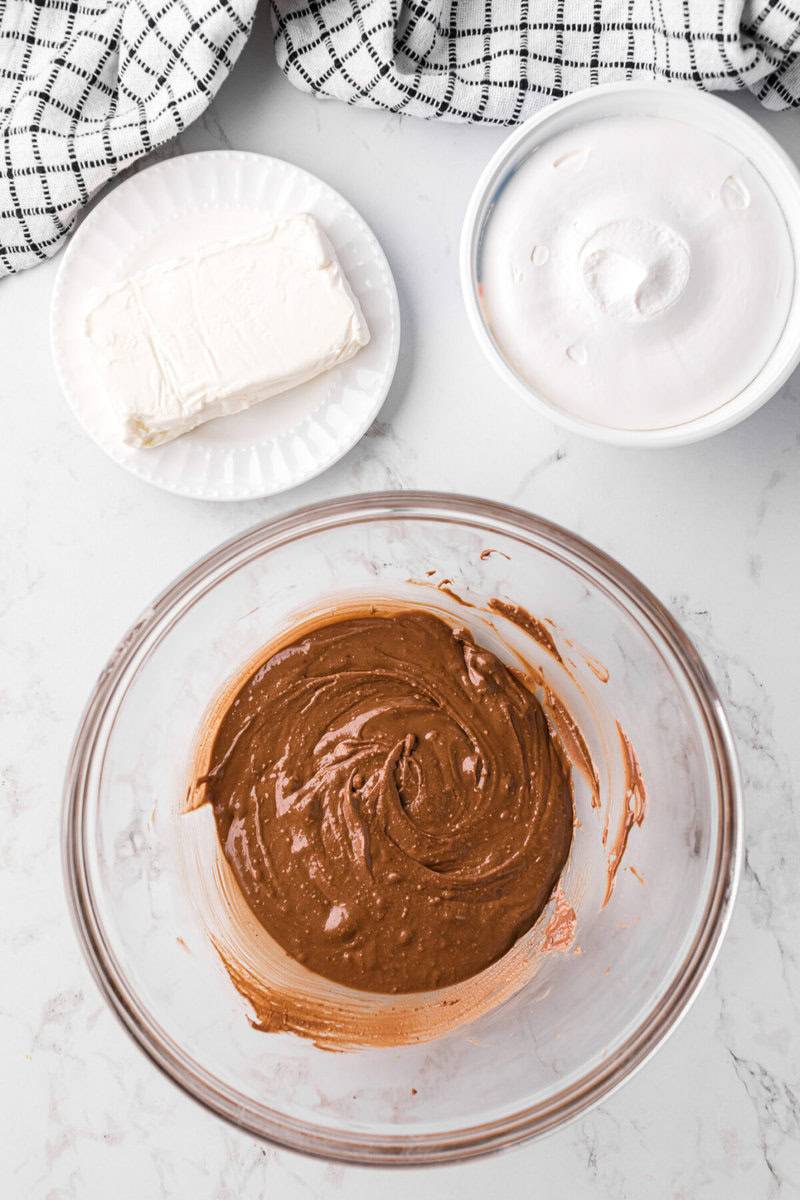 melted Reese's cups in glass bowl with cream cheese and whipped topping nearby.