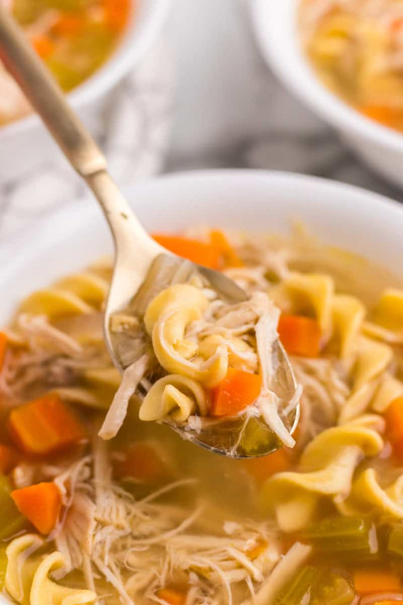 using a spoon to eat the chicken noodle soup.
