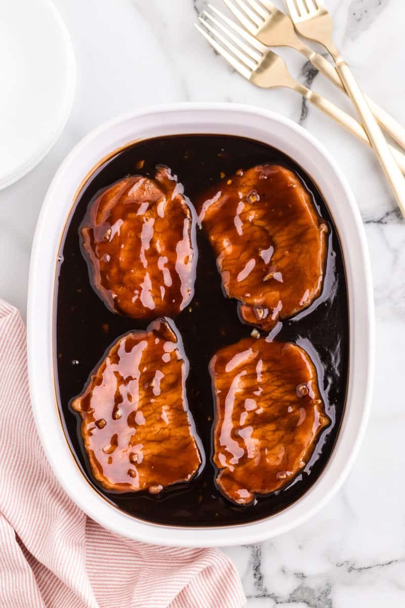 four pork chops in baking dish covered in teriyaki sauce.