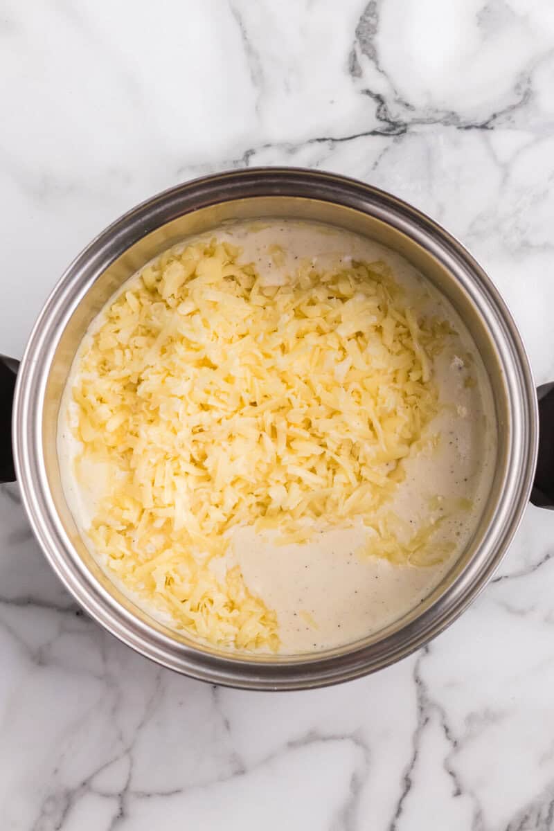 adding the shredded white cheddar cheese to the sauce.