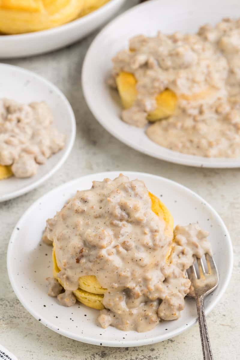 Sausage Gravy on top of a biscuit on a white plate.
