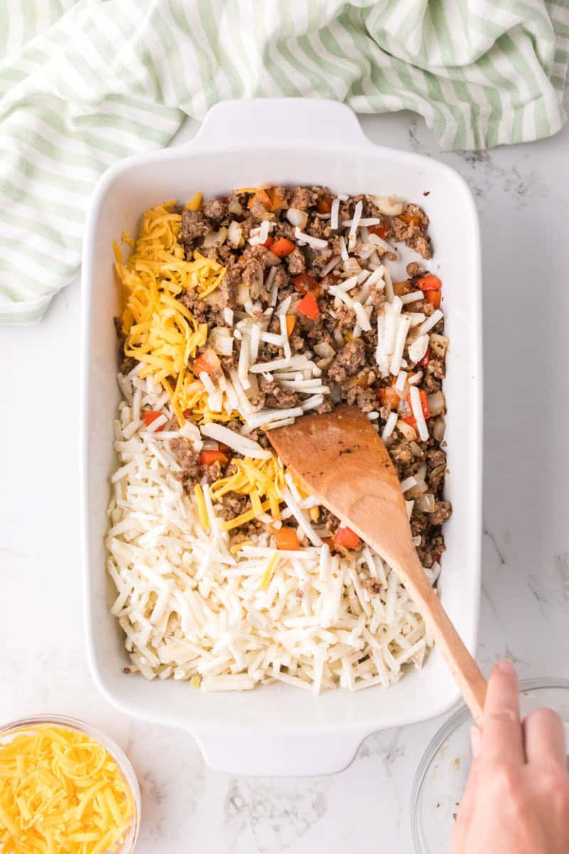 adding the sausage mix, potatoes and cheese to the casserole dish.