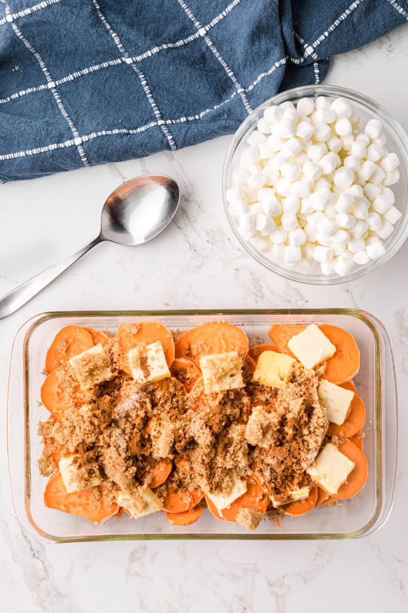 butter, brown sugar and spices on top of the yams in the casserole dish.