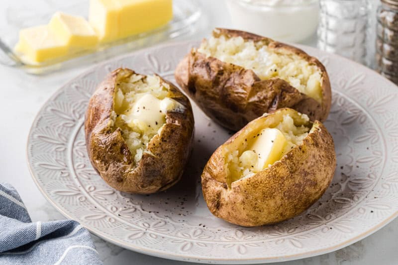 three baked potatoes on a white serving plate with butter.