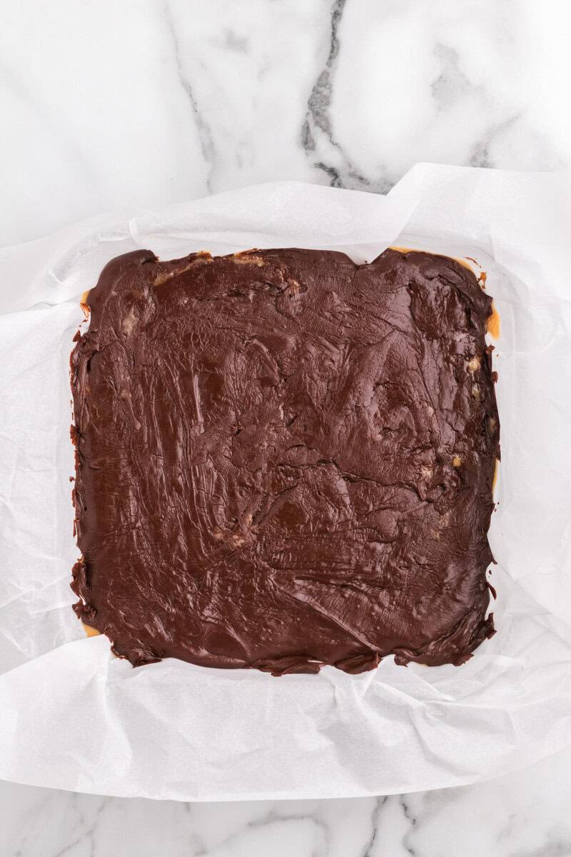 spreading the chocolate fudge layer on top of the peanut butter layer.