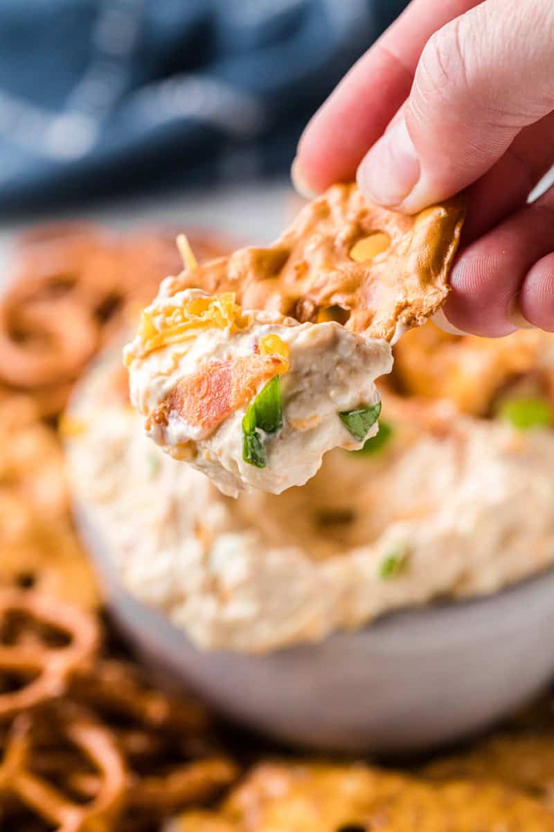 closeup of a pretzel with dip on it in hand.