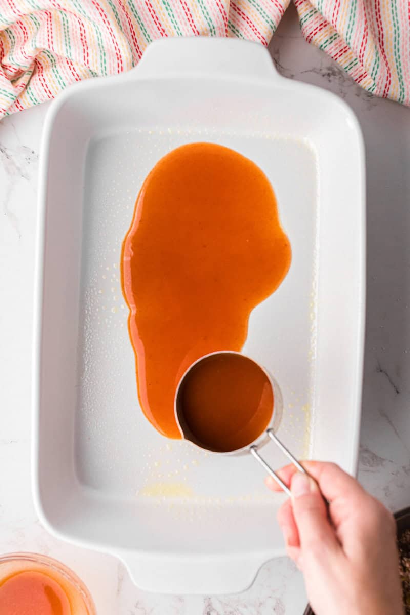 pouring enchilada sauce on to the bottom of the baking dish.