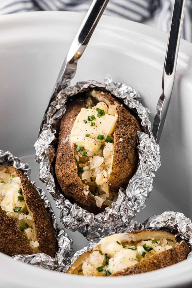 using tongs to serve the baked potatoes.