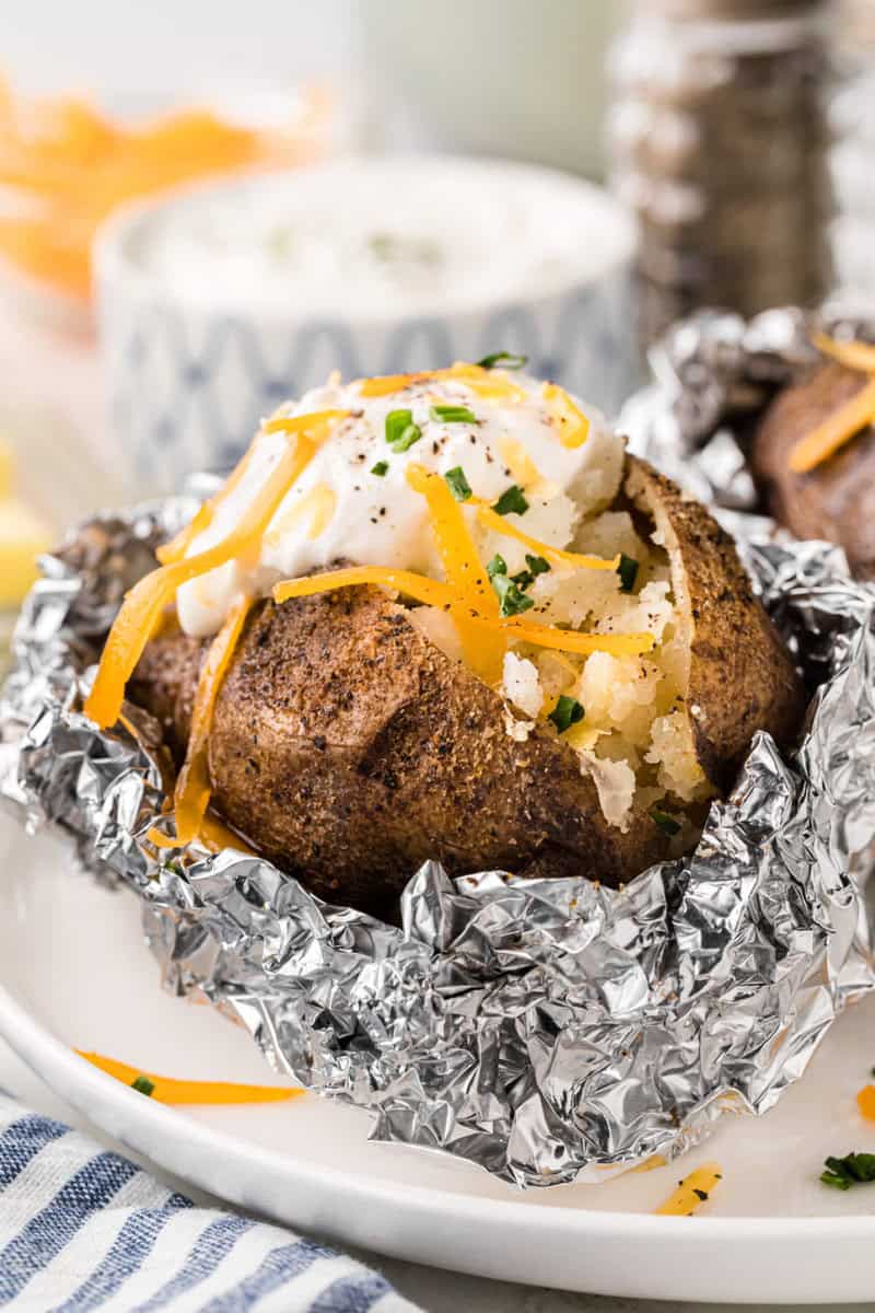 closeup of a baked potato topped with sour cream and cheese.