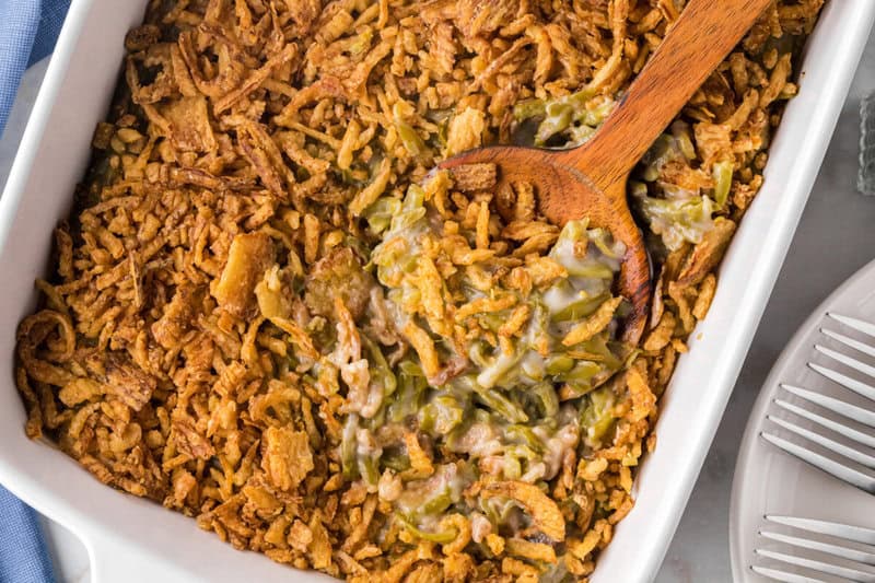 closeup of the Green Bean Casserole in white casserole dish being served with a wooden spoon.