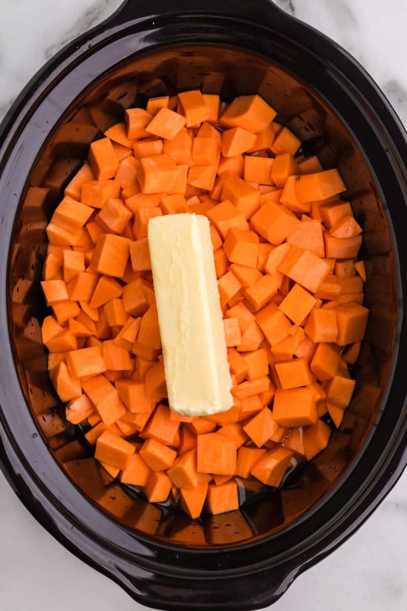 sweet potatoes in the bottom of the slow cooker with a stick of butter on top.