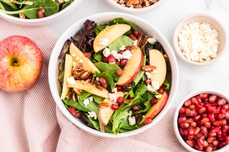 Thanksgiving Salad in white bowl with ingredients for the salad around it.