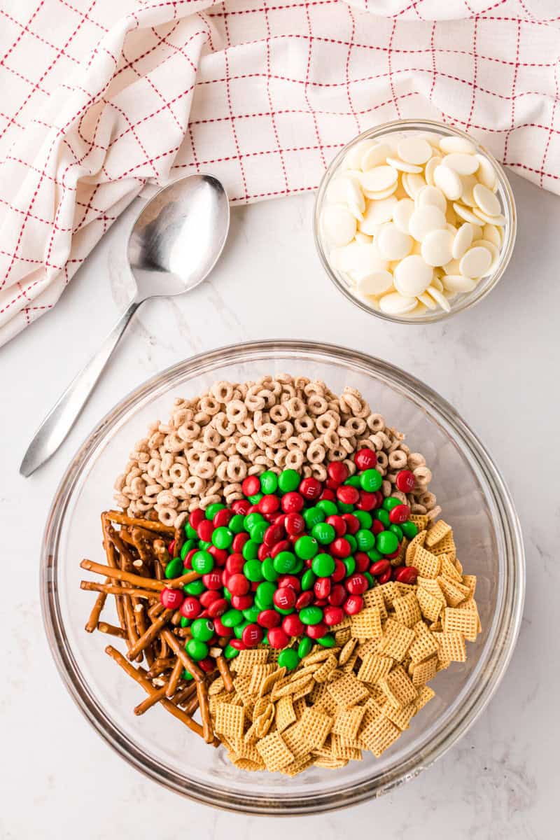 ingredients for the Christmas Chex Mix in a large clear mixing bowl.