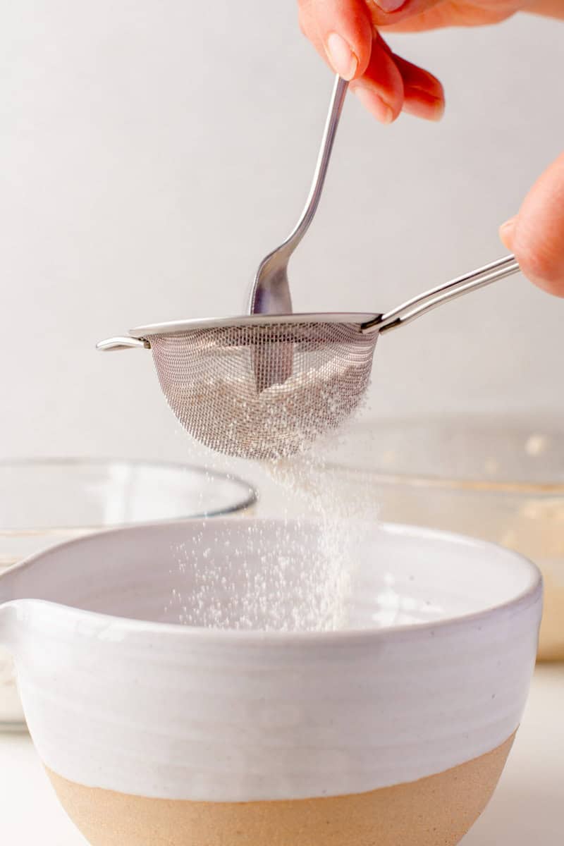 sifting the flour into a white bowl.
