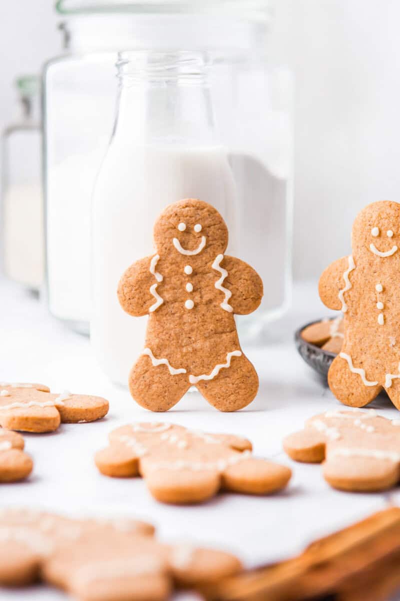 one gingerbread man standing up in front of a glass of milk.