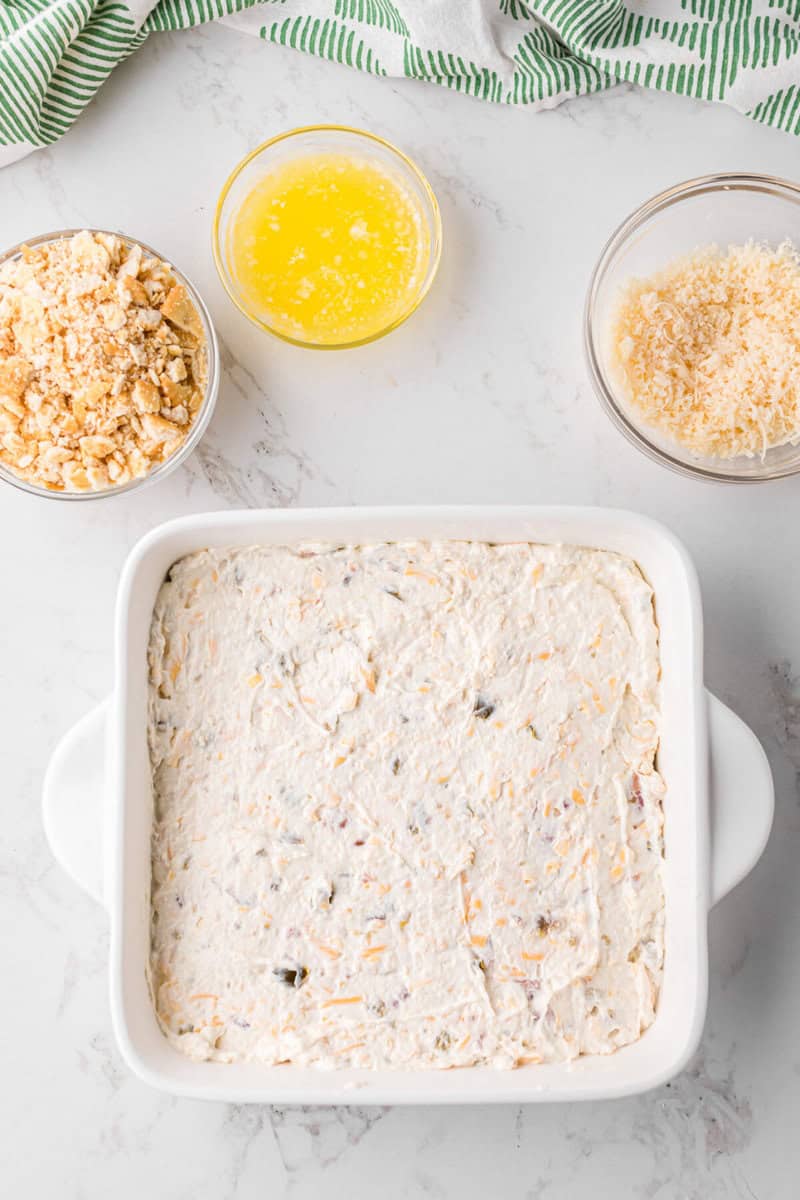 the dip in a white casserole dish with the topping ingredients in bowls beside the dish.