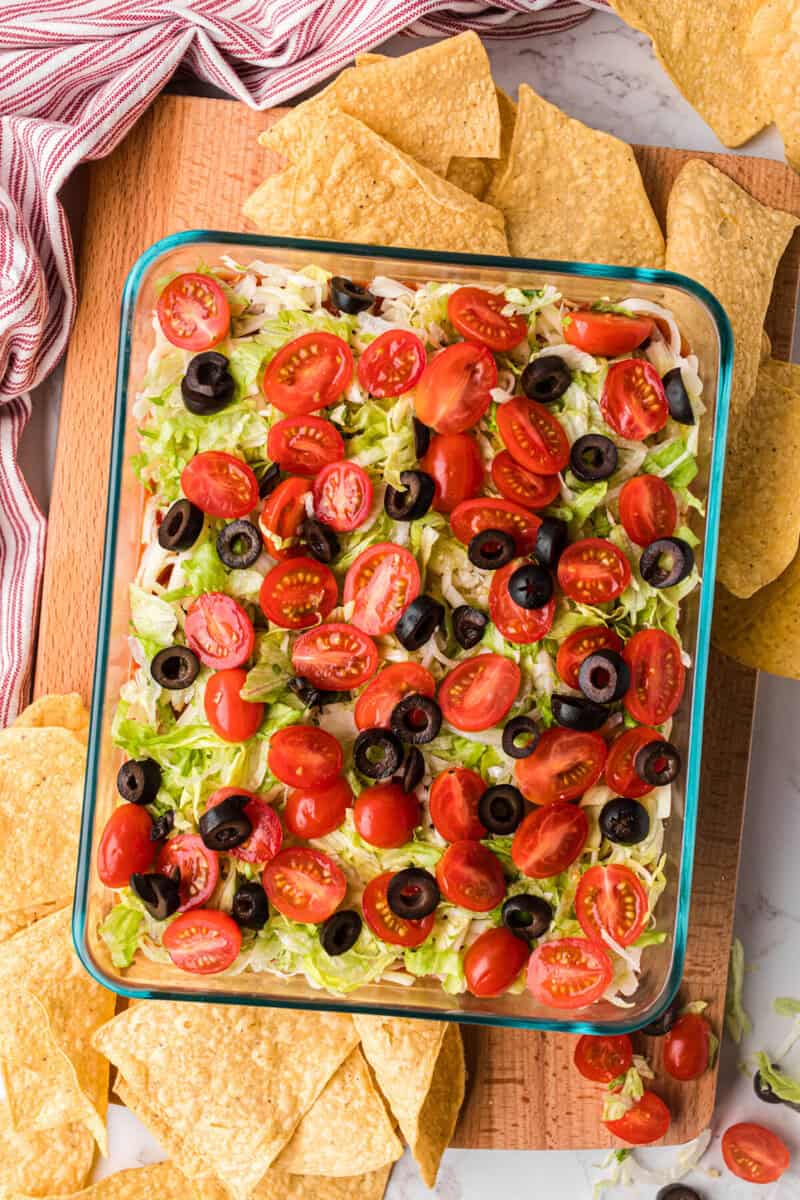 7 Layer Dip in the casserole dish with tortilla chips around it.