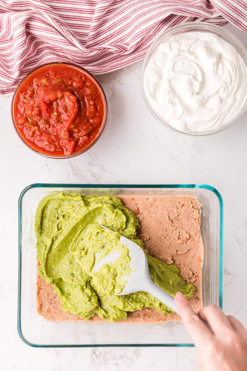 spreading the guacamole layer on top of the refried beans.