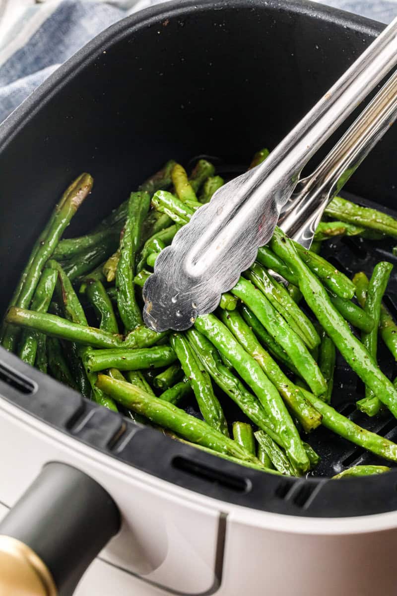 using tongs to serve the green beans.