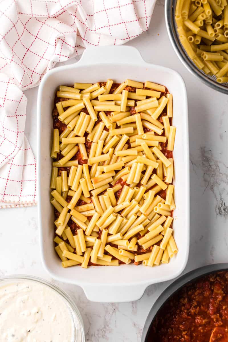 laying the sauce and the ziti in the baking dish.