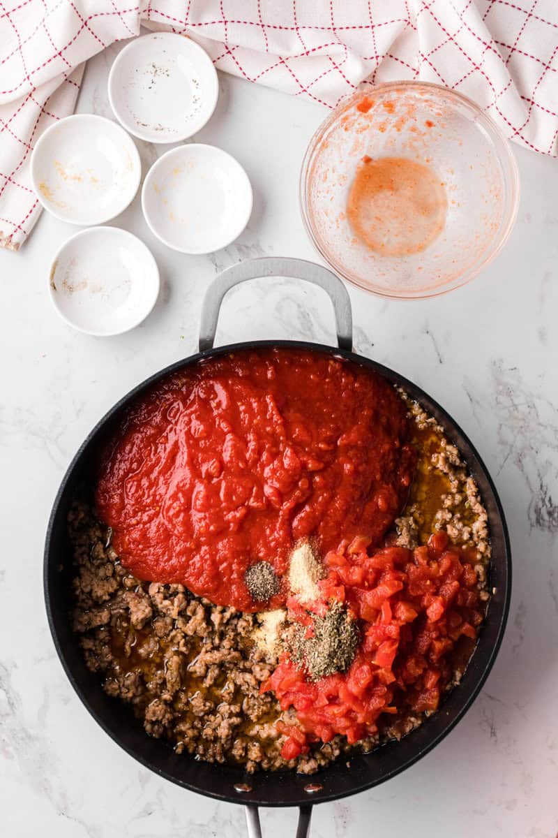 adding the seasonings and tomatoes to the meat to make the sauce.
