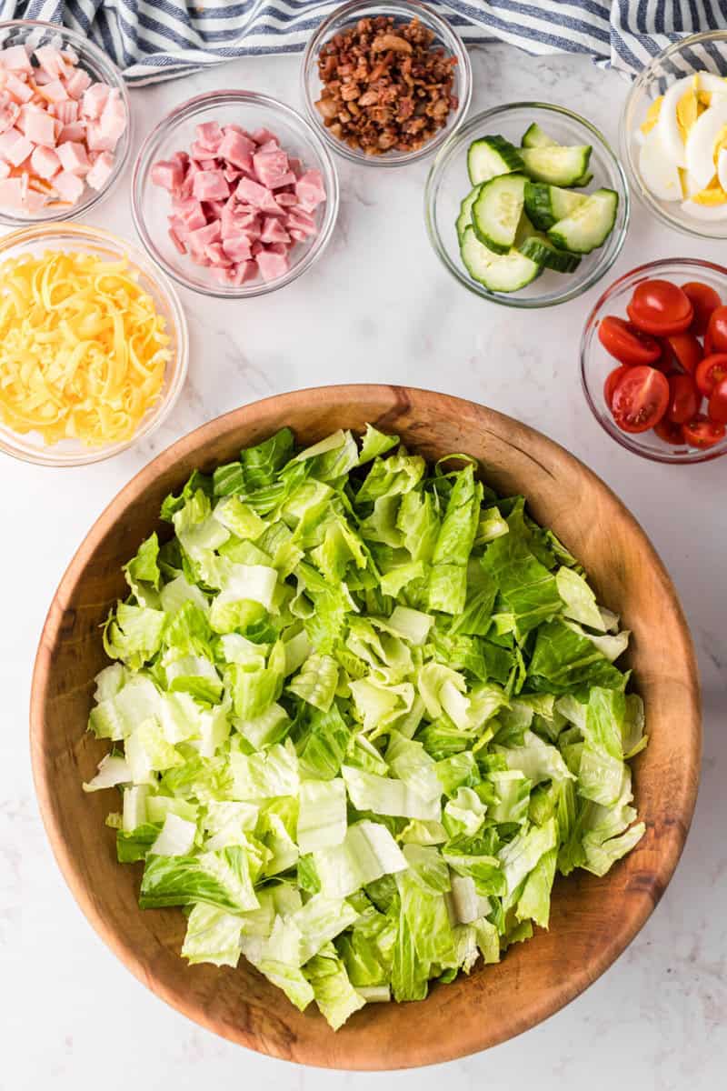 building the Chef Salad starting with the lettuce in the large wooden bowl.