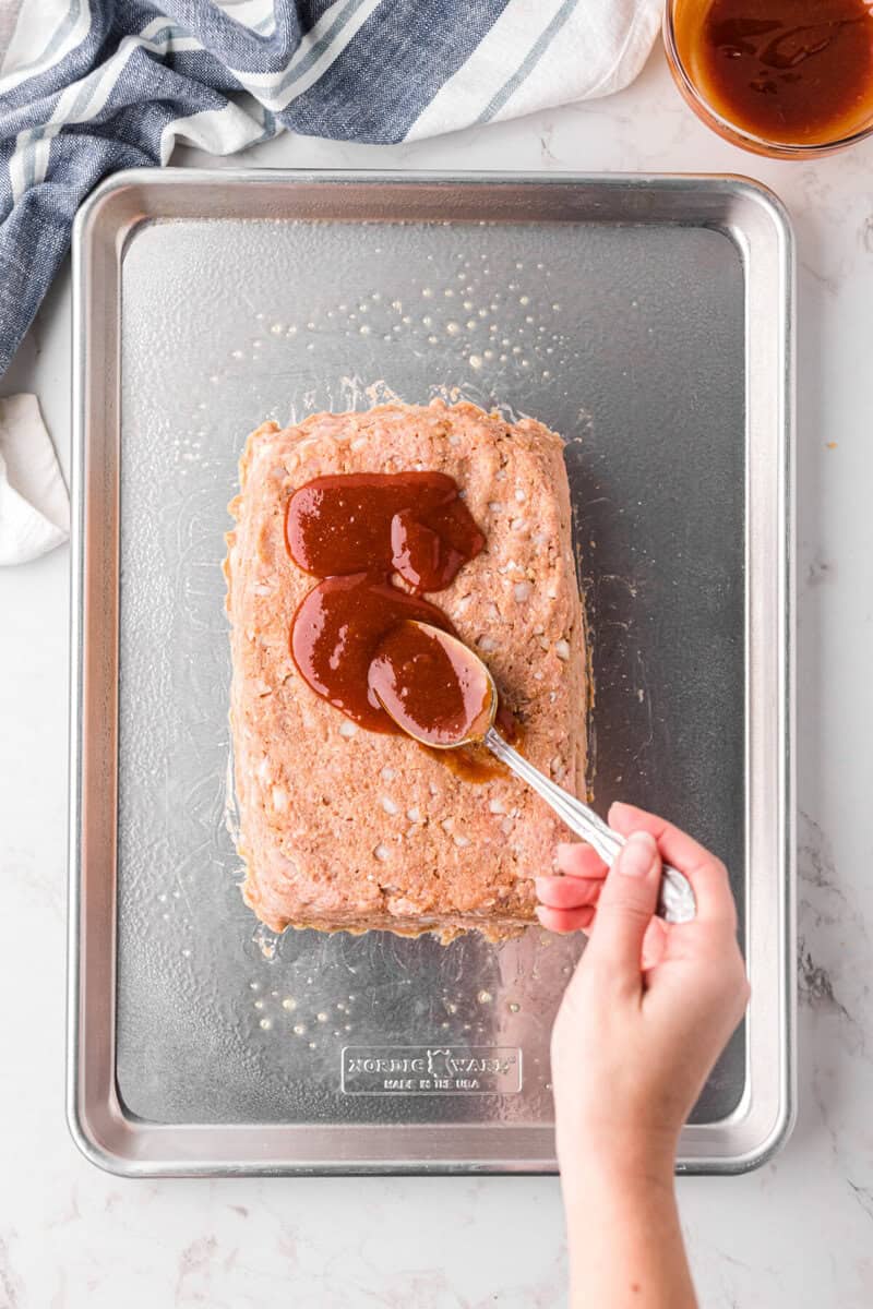 spreading the ketchup glaze on top of the turkey meatloaf before baking.
