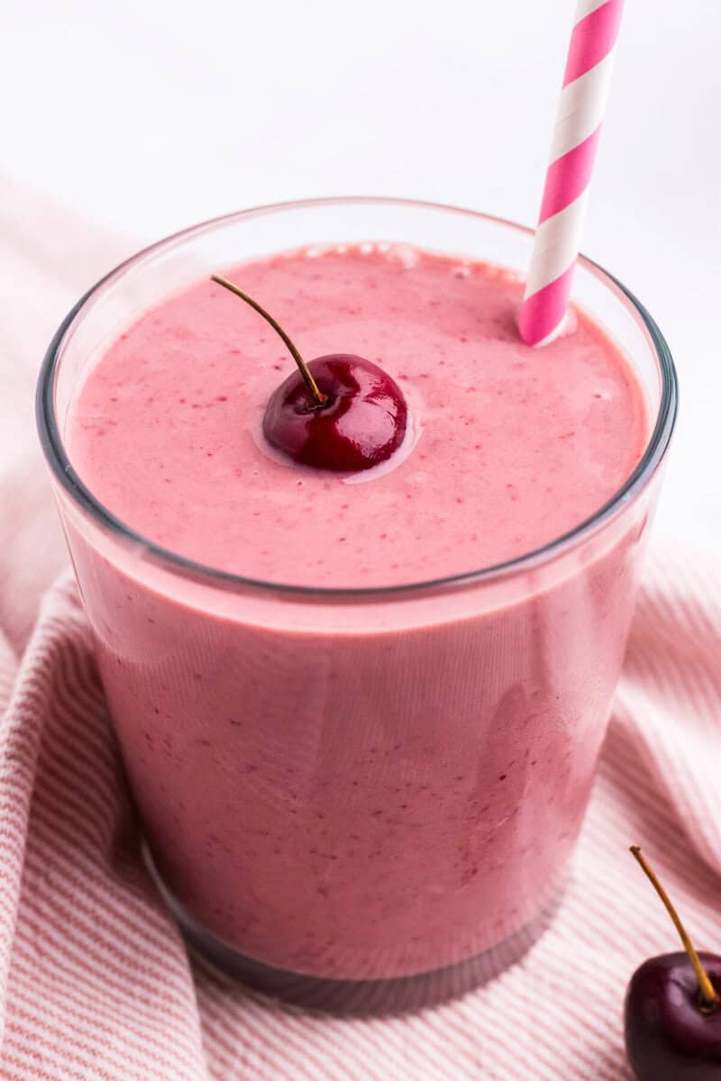 glass of the cherry smoothie with a cherry on top.