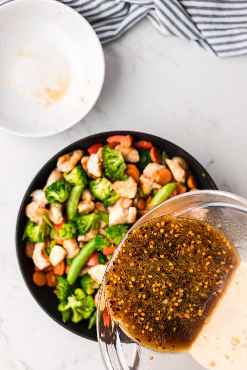 pouring the sauce over the stir fry.