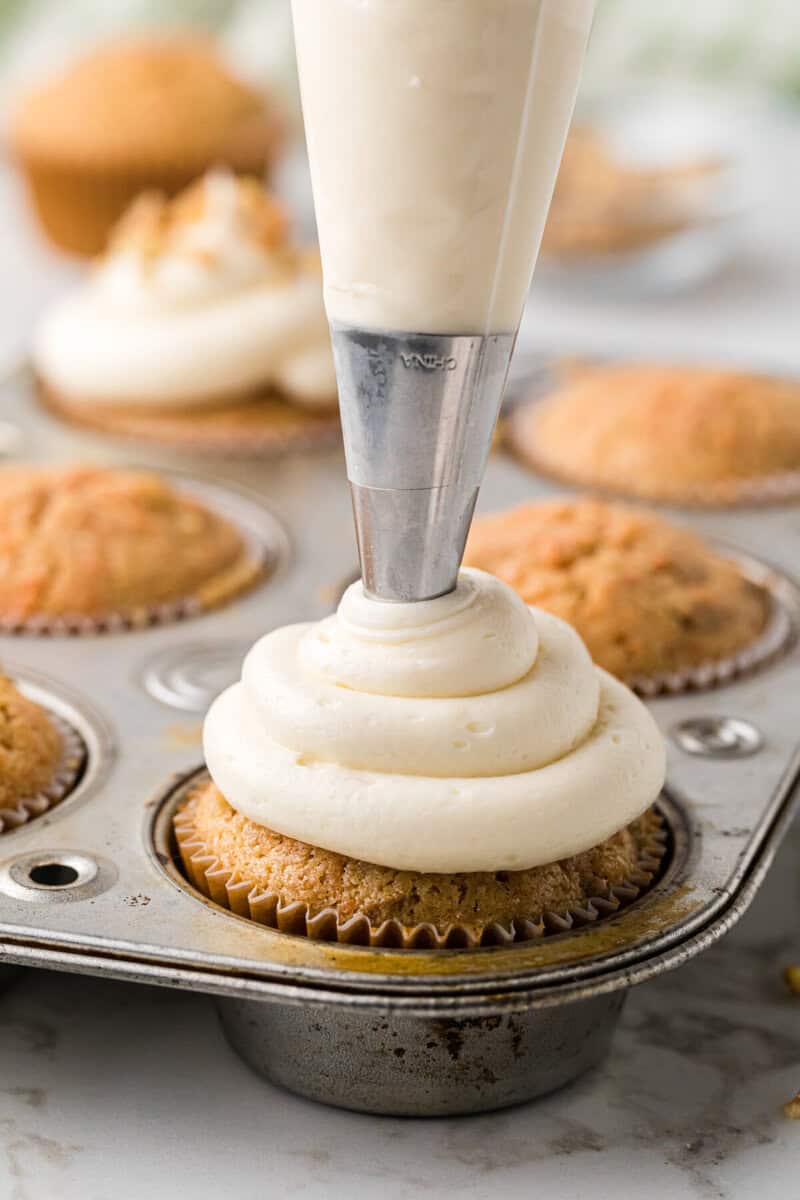using a piping bag to frost the cupcakes.