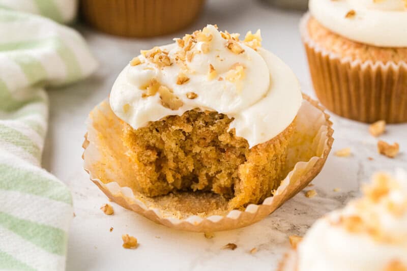 closeup of a carrot cake cupcake with a bite taken out of it.